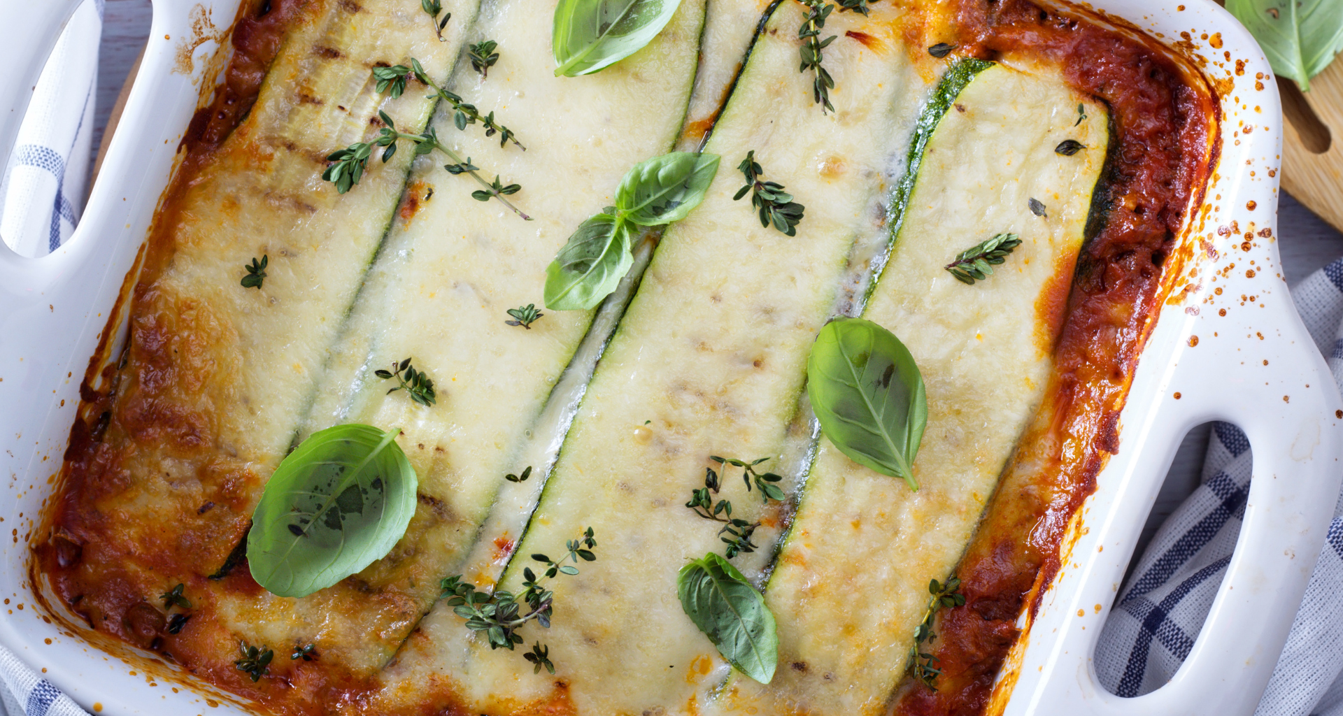 Zucchini lasagna in a white casserole dish with melted cheese and basil