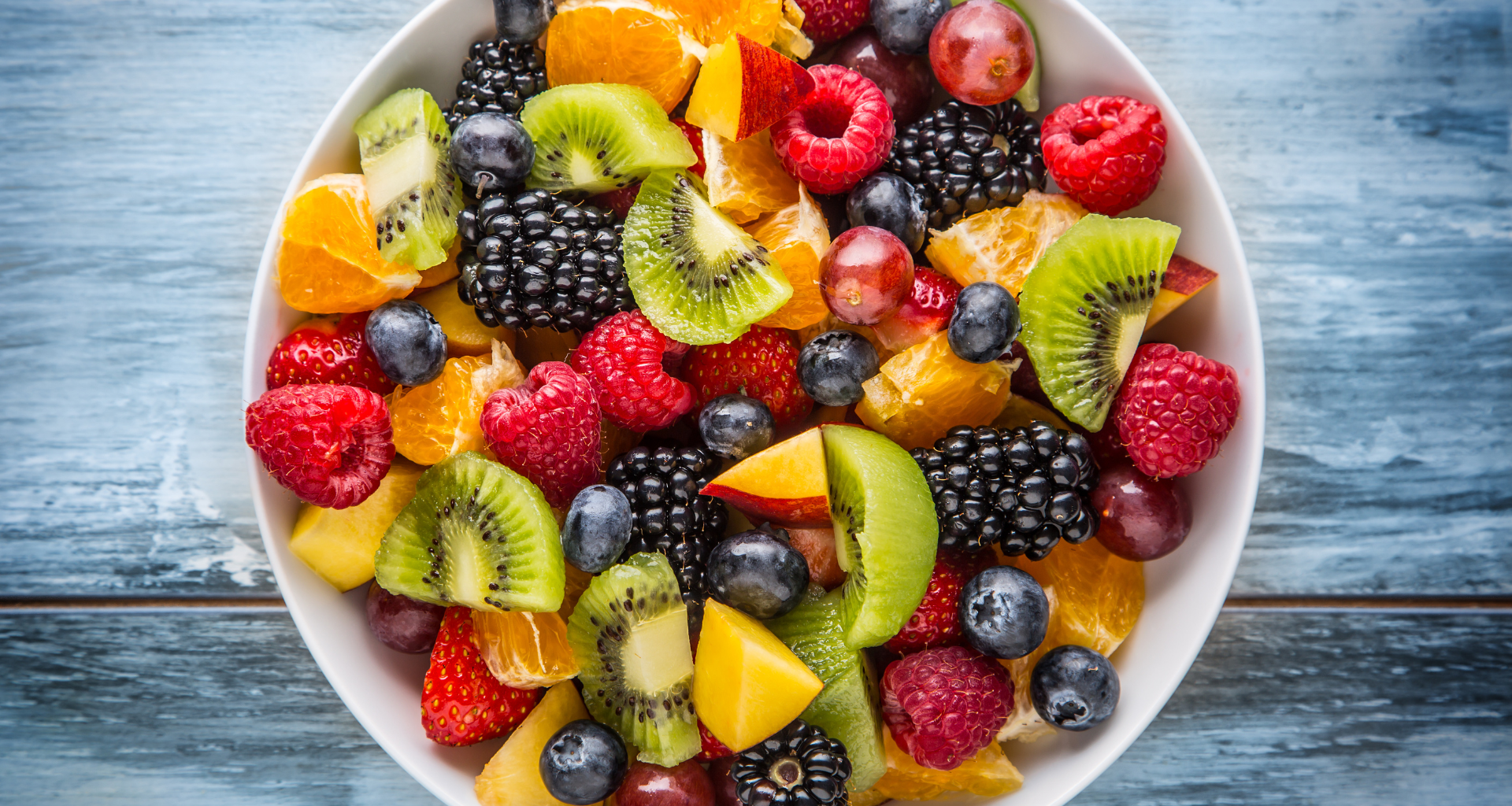 Colorful fresh fruit salad in white bowl on rustic blue wood background