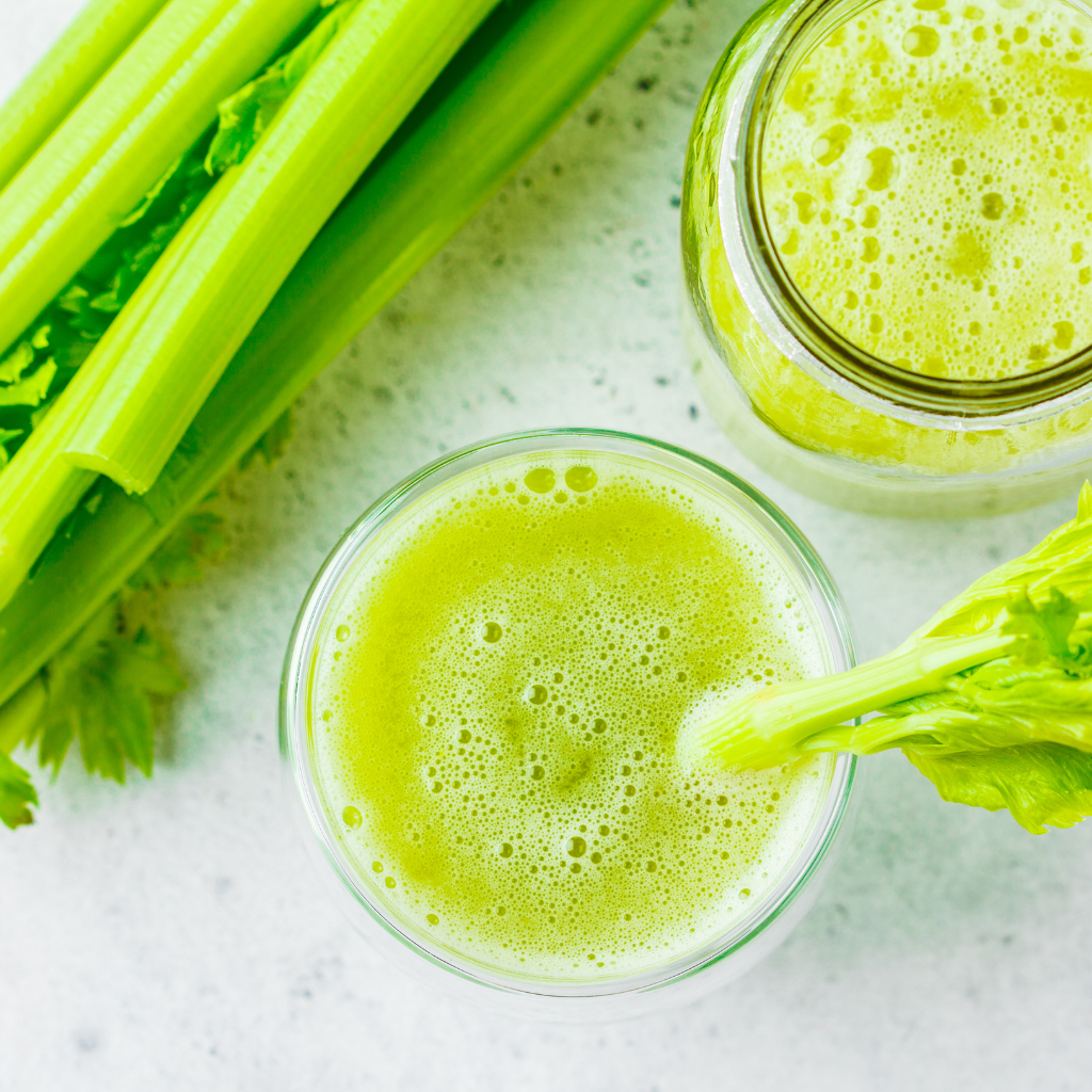 A glass of celery juice with sliced celery stalks in the background